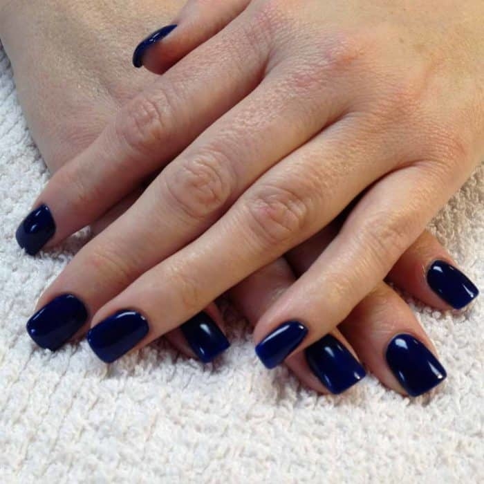 Dark blue gel polish on woman toenail with black shoes